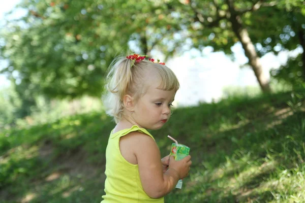 Ξανθό κοριτσάκι πίνοντας χυμό με άχυρο屋外公園で彼女のおもちゃの車を運転の少女 — Φωτογραφία Αρχείου