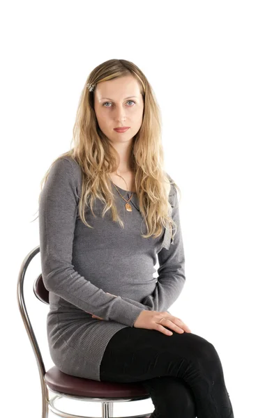 Mädchen mit langen Haaren sitzt auf einem Stuhl und schaut uns an, auf weißem Hintergrund — Stockfoto