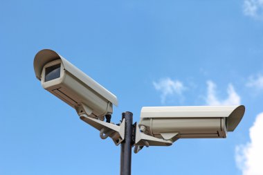Mavi gökyüzüne karşı iki güvenlik kamerası