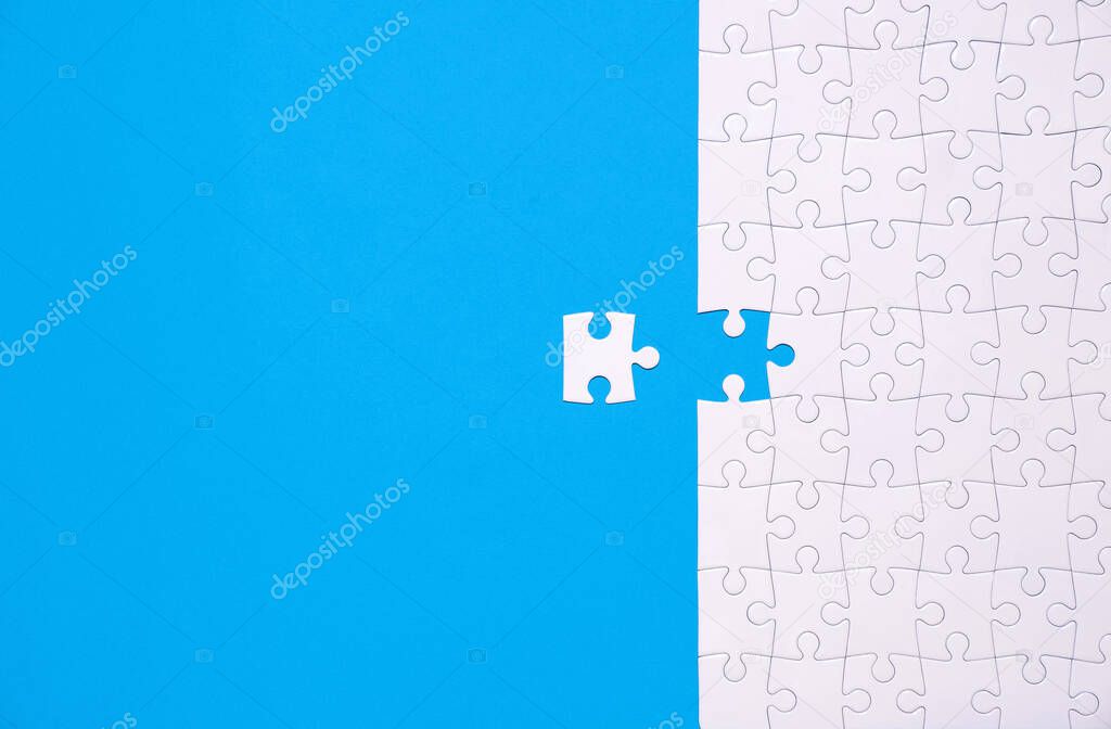 Unfinished white jigsaw puzzle isolated on blue background with copy space
