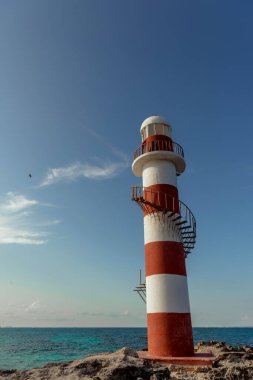 Beyaz-kırmızı bir deniz fenerinin tepesinde mavi gökyüzüne karşı bir uçak. Meksika.