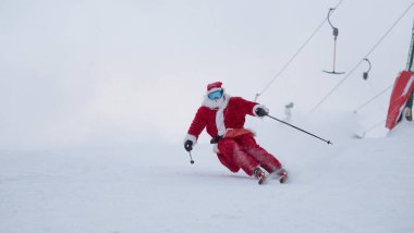 Noel Baba alp kayakçısı karlı orman kayak merkezinde yokuş aşağı kayak yapıyor.