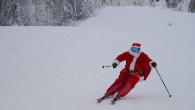 Noel Baba alp kayakçısı karlı orman kayak merkezinde yokuş aşağı kayak yapıyor.