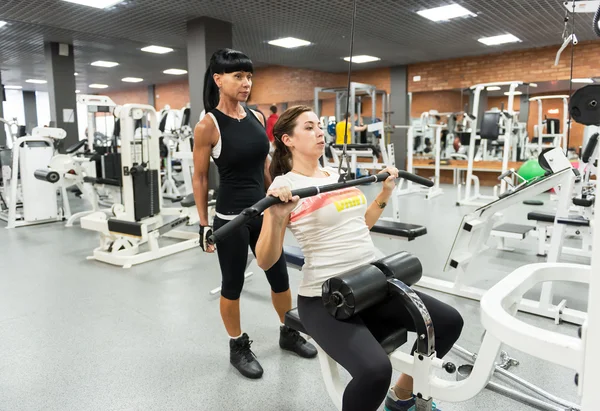 Ung kvinna med en instruktör i gymmet — Stockfoto