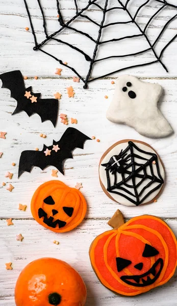 Halloween food and decorations, vertical top view. Halloween cookies, ghost, web and bats, flat lay. Funny objects on white wooden table for Hallowen. Concept of Happy Halloween, autumn and horror.