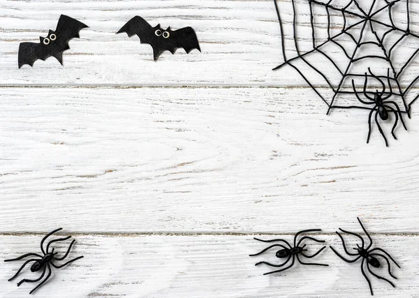 Halloween background with spiders, web and bats, top view. Halloween objects on white wooden table with space for text, flat lay. Minimalist Hallowen decorations. Happy Halloween and horror concept.