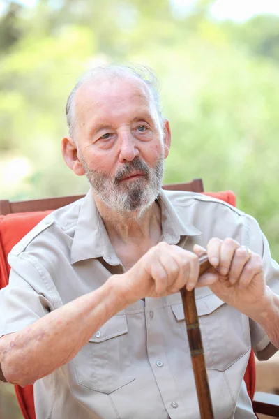 Älterer Mann mit Gehstock sitzt im Garten — Stockfoto