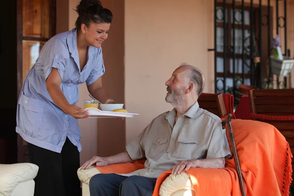 Hemşire veya yerleşim ana kıdemli adama yiyecek vererek yardımcı — Stok fotoğraf