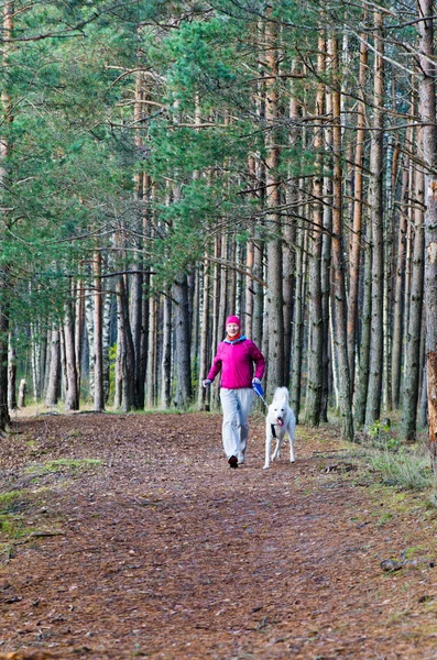 Kvinnan med en hund som kör i en forest park — Stockfoto