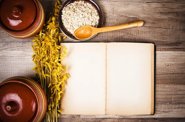 Farinha de aveia e um velho livro de receitas na mesa da cozinha — Fotografia de Stock
