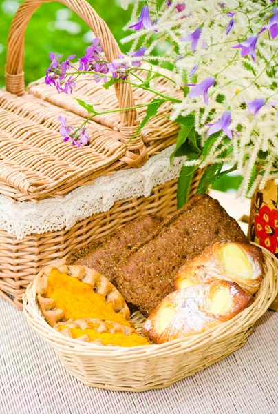 Buns in a wicker basket and a bouquet of field flowers close-up — Stock Photo, Image