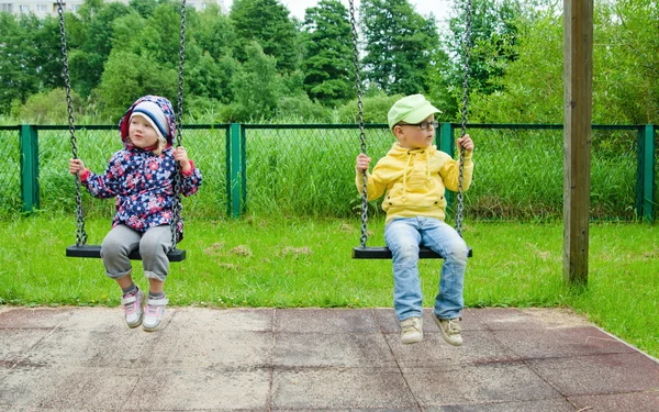 Young children, a boy with a girl swinging on a swing — Stock Photo, Image