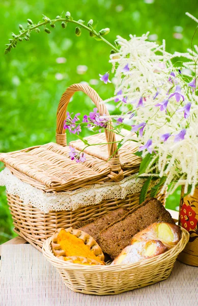 Brötchen im Weidenkorb und ein Strauß Feldblumen — Stockfoto