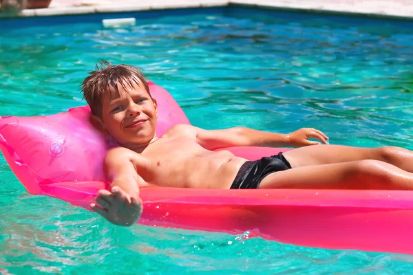 Sonriente chico se encuentra en el colchón rosa en la piscina —  Fotos de Stock