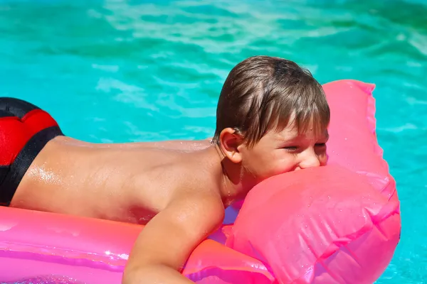 Boy gülümseyerek pembe şişme havuz içinde yatıyor. — Stok fotoğraf