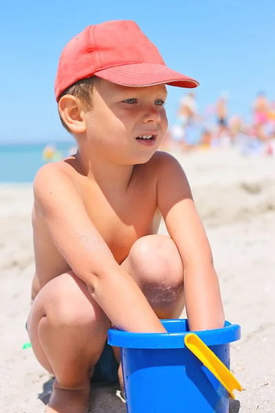 Menino bonito com um balde na praia junto ao mar — Fotografia de Stock