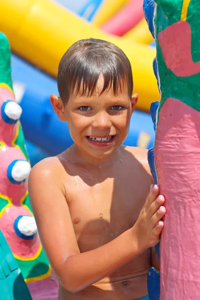 Ragazzo sorridente in un parco acquatico vicino agli scivoli gonfiabili — Foto Stock