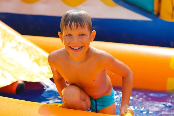 Lachende jongen in het water in de buurt van glijbaan. — Stockfoto