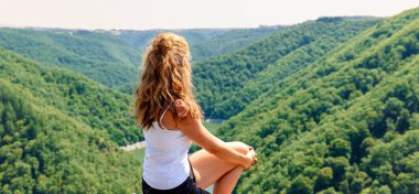 Woman sitting on rock looking at panoramic view of forest mountain (dordogne in france)