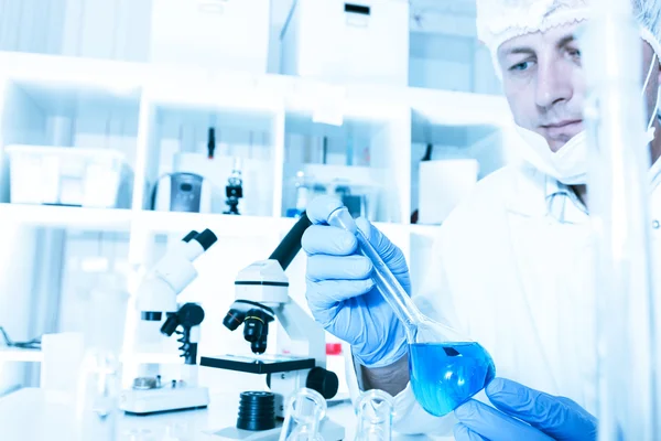 Scientist working in the lab, in protective mask , examines a with liquid — Stock Photo, Image