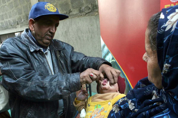 Здоров'я працівника адмініструє вакцини проти поліомієліту крапель з дитиною під час кампанії проти поліомієліту Стокове Зображення