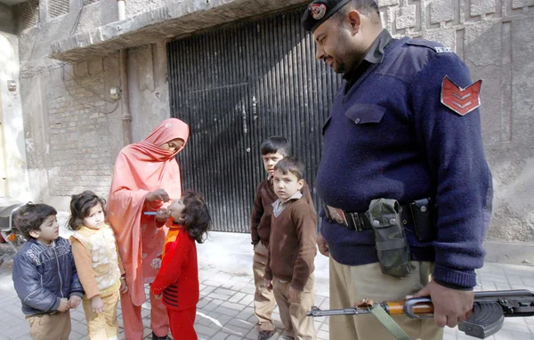 Un trabajador de la salud administra las gotas de la polio-vacuna a un niño durante la campaña contra la polio mientras que el funcionario de policía se mantiene alerta para vigilar Fotos de stock libres de derechos