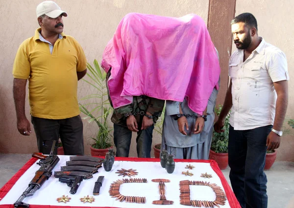Сотрудники полиции заявили, что обвиняемые активисты несуществующего Tehreek-e-Taliban (с закрытыми лицами) и изъятое оружие — стоковое фото