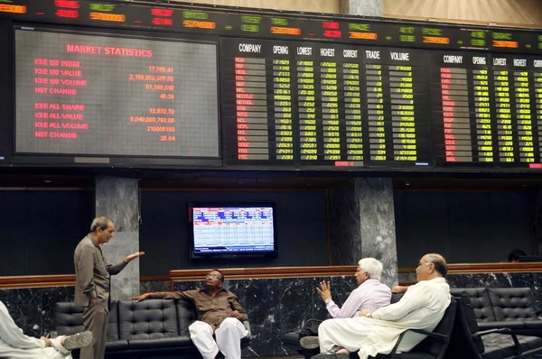 Corretores de bolsa sentar perto de uma placa de índice mostrando um aumento acentuado das ações durante a sessão de negociação na Bolsa de Valores de Karachi Imagens De Bancos De Imagens