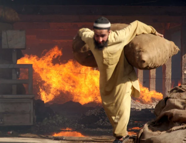 El hombre lleva una bolsa de cebollas para mantenerla a salvo del fuego que estalló en un almacén en New Sabzi Mandi —  Fotos de Stock