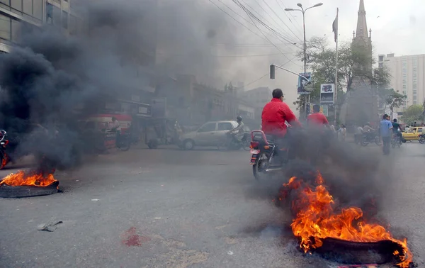 Commuters pass near burning tyres that ablaze by angry protesters during protest demonstration of residents of Kharadar against targeted operation — Stock Photo, Image