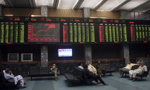 Traders sit beneath an electronic display board showing the ongoing development of various stock shares at the Karachi Stock Exchange (KSE) — Stock Photo, Image