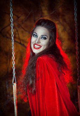 Salıncağın üzerindeki kırmızı pelerin içinde Halloween kadın gülüyor