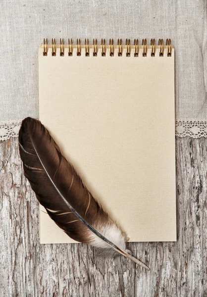 Notebook, feather and linen fabric on the old wood — Stock Photo, Image