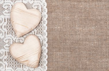 Burlap background with lacy cloth and wooden hearts