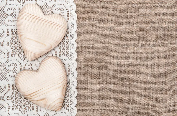 Burlap background with lacy cloth and wooden hearts — Stock Photo, Image