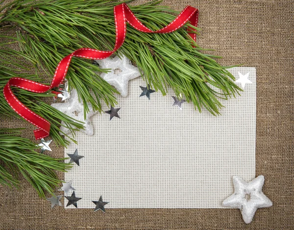 Kerstkaart met fir branch, sterren en rood lint op jute — Stockfoto