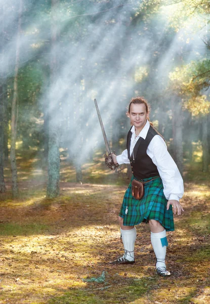 Hombre escocés guapo con espada en el bosque — Foto de Stock