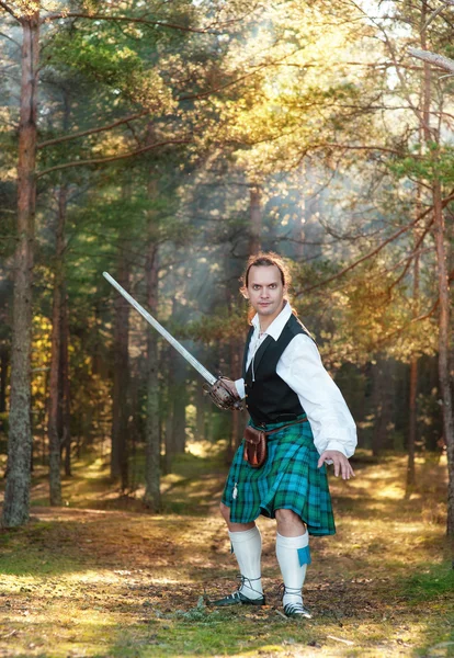 Hombre escocés guapo con espada en el bosque — Foto de Stock