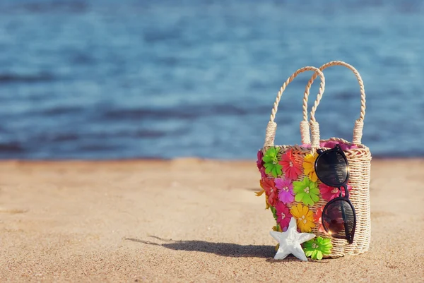 Wicker bag and sunglasses on the beach — Stock Photo, Image