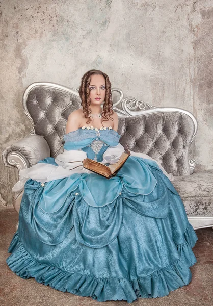 Mulher bonita em vestido medieval com livro no sofá — Fotografia de Stock