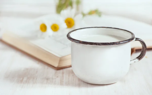 Milk in metal mug and chamomile flowers in open book — Stock Photo, Image