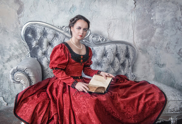 Beautiful woman in medieval dress on the sofa with book