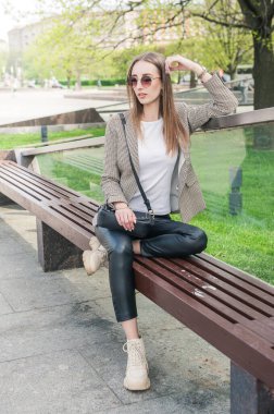 Güzel, genç, moda tarzı bir kadın gözlüklü, şehirde bankta oturuyor.