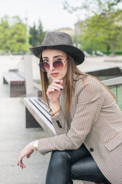 Şehirdeki bankta oturan şapkalı güzel, genç bir moda kadını.