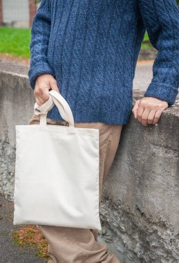 Beyaz boş tuval taşıyan şık bir adam açık havada alışveriş çantası taşıyor.