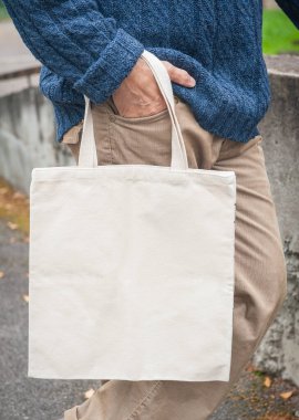 Beyaz boş tuval taşıyan şık bir adam açık havada alışveriş çantası taşıyor.