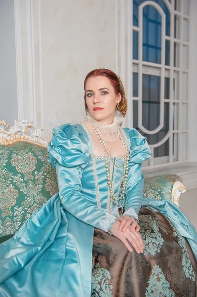 坐在沙发上的穿着中世纪风格蓝色衣服的年轻漂亮女人 — 图库照片