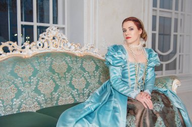 Ortaçağ tarzı mavi elbiseli güzel bir kadın kanepede oturuyor.