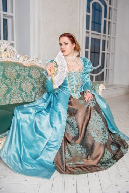 Ortaçağ tarzı mavi elbiseli, kanepede oturan genç ve güzel bir kadın.