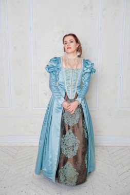 Ortaçağ tarzı mavi elbiseli güzel genç kadın odada duruyor.